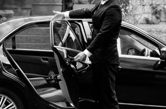 Professional chauffeur opening car door for VIP clients.