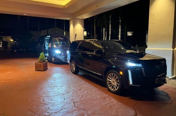 luxury ride for any occasion vista ca A sleek black SUV and a black Sprinter Van from VIP Ride 4 U parked under illuminated lights at the elegant entrance of a modern hotel in Vista, CA, showcasing upscale chauffeur-driven transportation for premium travel experiences.